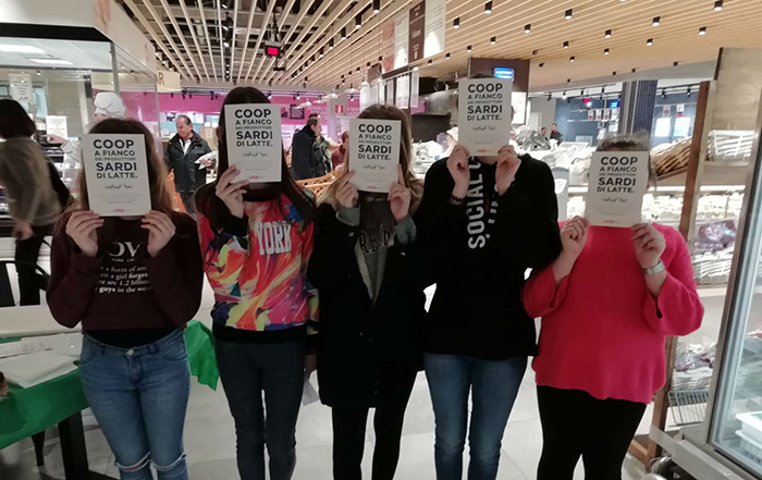 Ragazzi che tengono davanti al viso il volantino: Coop a fianco dei produttori sardi di latte