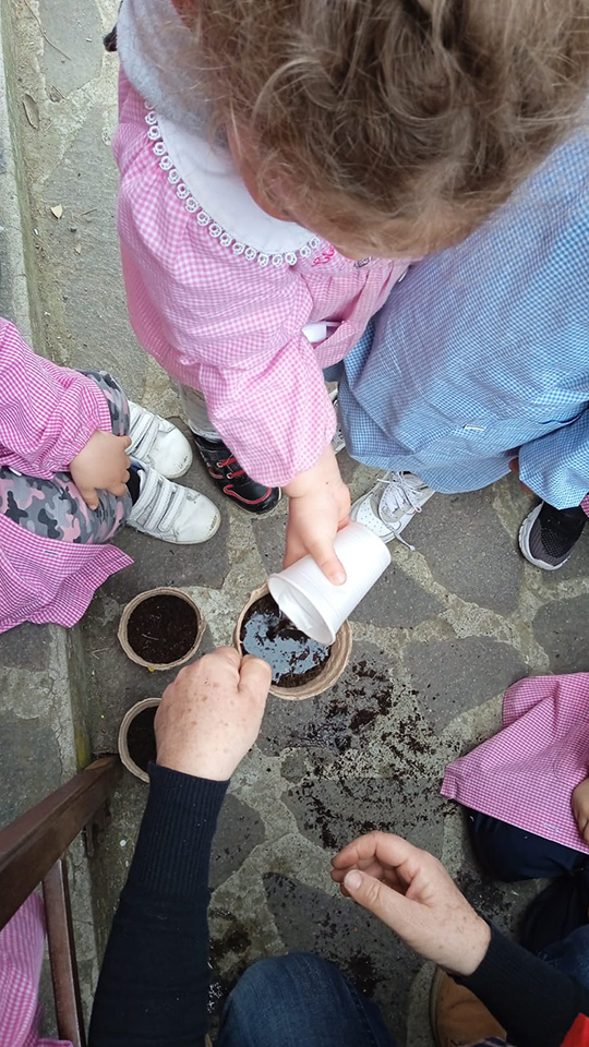 Bambini innaffiano i loro vasetti pieni di terra