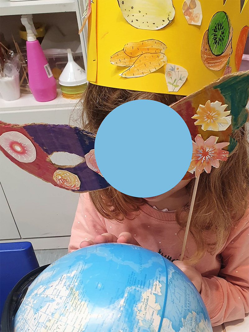 Bambina con maschera di carnevale che guarda il mappamondo Bambina con maschera di carnevale che guarda il mappamondo