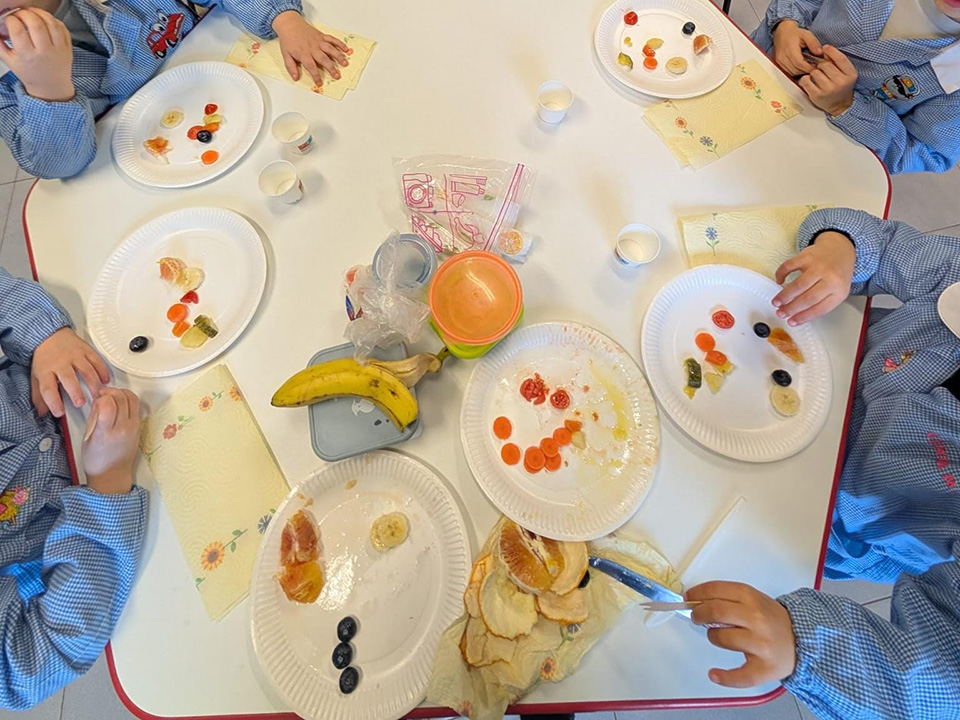 foto di bambini intorno a un tavolo con piatti contenenti frutta e verdura